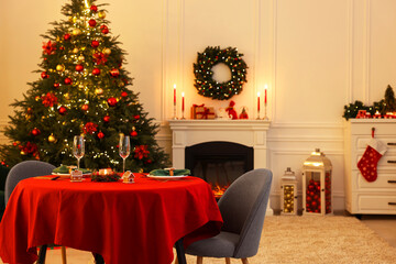 Cozy living room with Christmas tree near fireplace and table served for celebration. Interior design
