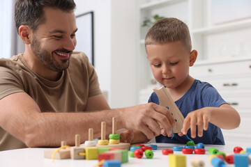 Motor skills development. Father and his little son playing with wooden lacing toy at white table...