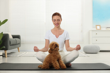 Happy young woman practicing yoga on mat with her cute dog at home