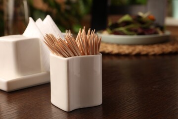 Holder with many toothpicks on wooden table, closeup. Space for text - obrazy, fototapety, plakaty