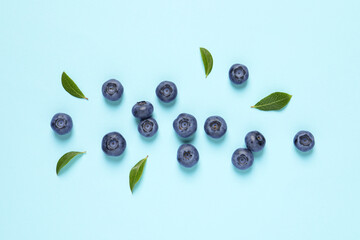 Tasty fresh blueberries with green leaves on light blue background, flat lay