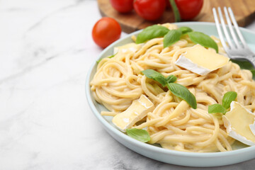 Delicious pasta with brie cheese and basil leaves on white marble table, closeup. Space for text