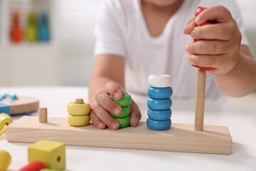 Motor skills development. Little boy playing with stacking and counting game at table indoors, closeup