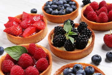 Tartlets with different fresh berries on white wooden table, closeup. Delicious dessert