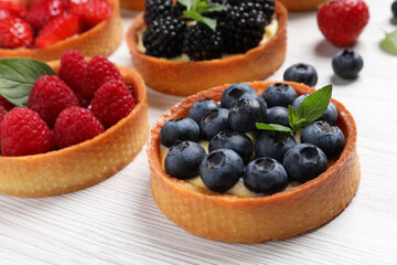 Tartlets with different fresh berries on white wooden table, closeup. Delicious dessert