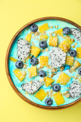 Delicious smoothie bowl with fresh fruits, blueberries and oatmeal on yellow background, top view