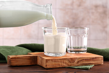 Pouring milk from bottle into glass at wooden table, closeup