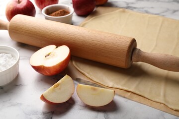Fresh dough, rolling pin and ingredients on white marble table, closeup. Making apple pie