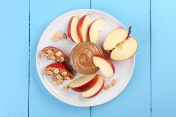 Fresh red apple with peanut butter and nuts on light blue wooden table, top view