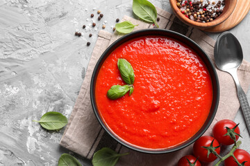 Delicious tomato cream soup served on grey textured table, flat lay. Space for text
