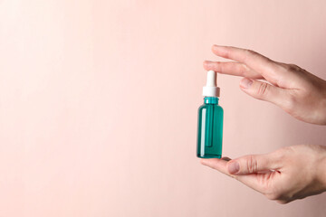 Woman with bottle of cosmetic serum on light pink background, closeup. Space for text