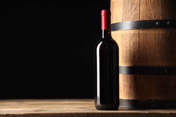 Bottle of delicious wine and wooden barrel on table against black background. Space for text