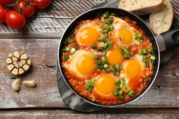 Delicious Shakshuka in frying pan served on wooden table, flat lay