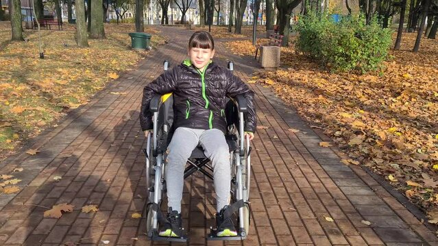 Little beautiful girl in a wheelchair outdoors. Girl rides in wheelchair in park in autumn