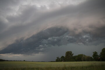 A massive storm cloud casts a dark shadow over a serene grassy field, creating an ominous atmosphere.