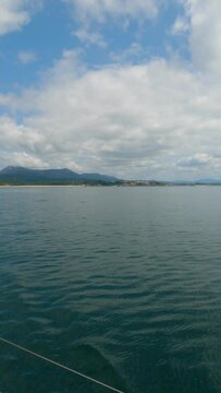 Scenic slow-motion cruise in R&iacute;a de Arousa: Blue seas, Coroso Beach, Ribeira, and glimpses of playful dolphins under a summer sky with scattered clouds.