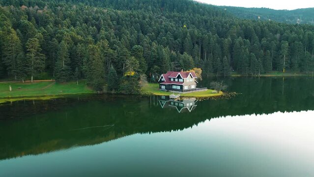 The drone in the forest moves through the trees and sees the image of the house on the lake. Gorgeous autumn colors. Bolu, Turkey.