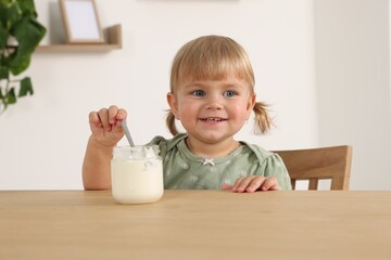Cute little child eating tasty yogurt with spoon from jar at wooden table