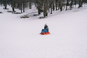 Fototapeta na wymiar Smiling man in sunglasses going down hill on sled