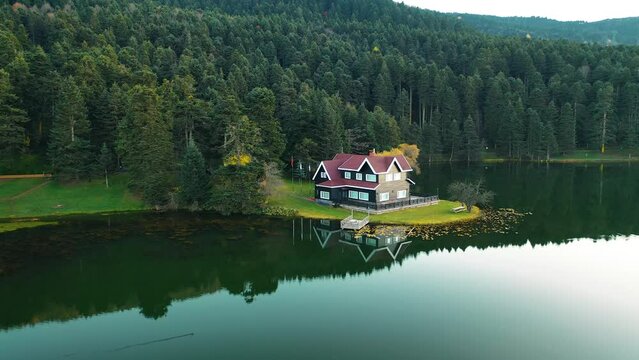 The drone in the forest moves through the trees and sees the image of the house on the lake. Gorgeous autumn colors. Bolu, Turkey.