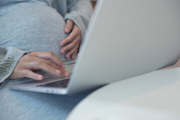 Pregnant woman working on laptop. Cropped image of pregnant businesswoman sitting at table typing on laptop at her working place in office