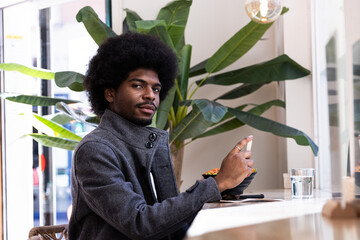 Young african boy with afro hair is sited on a restaurant while he is eating a poke bowl.