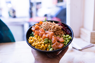 Focused photo of a caucasian hand holding a beautiful poke bowl with a los of nutrients.