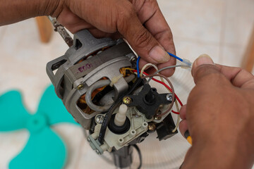 A technician checks the wiring of a defective old oscillating electric fan. Cleaning and repairing an electric stand fan. Top view.