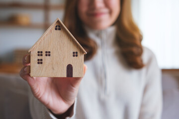 Closeup image of a young woman holding and showing a wooden house model