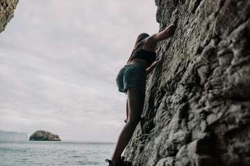 Sports Woman Climbing The Rock. Young woman With slim fit body climbing in volcanic basalt cave...
