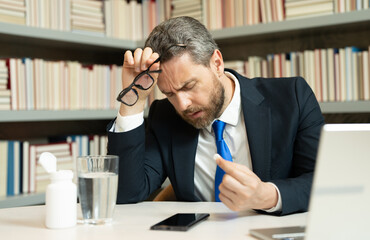 Sad man got migraine touches her head because of pain. Man manager with strong headache working on laptop. Overworked freelancer or manager at office. Stressed, tired man with headache.
