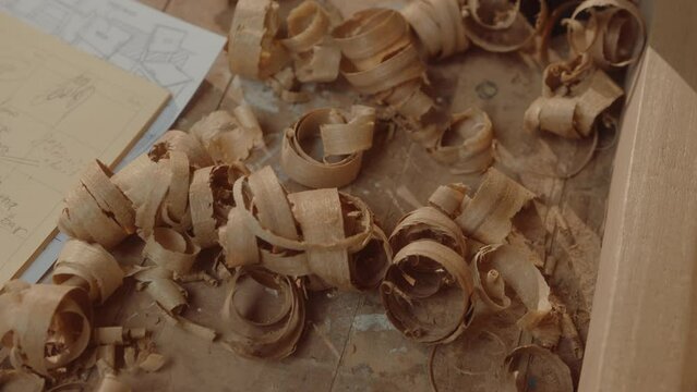 Curled wood shavings, notes on paper and furniture sketches on the workbench in the woodshop. Close-up shot, directly above view