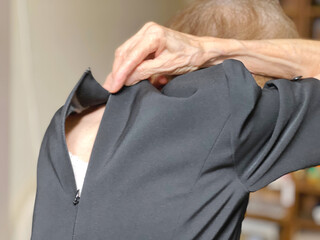 喪服の背中のファスナーを上げようとしている高齢女性の手元 - obrazy, fototapety, plakaty