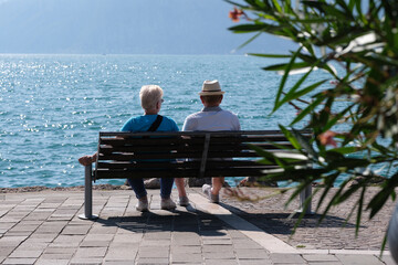 A family couple on a bench rear view in the background water, mountains, sky. An elderly couple on a bench near the water, rear view.