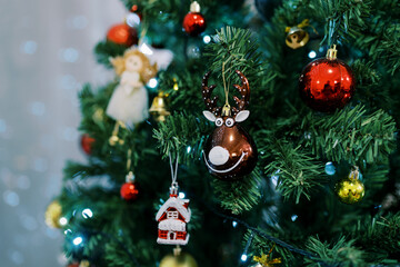 Deer figurine, a toy house and a red shiny ball hang on the branches of a Christmas tree