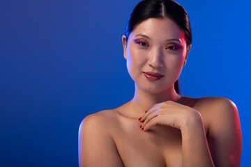Portrait of asian woman wearing purple eye shadow and red nail polish on blue background, copy space