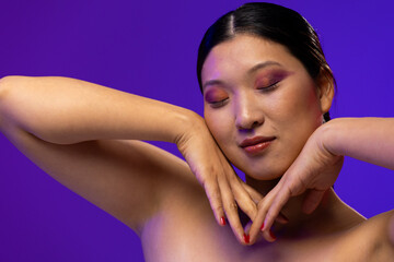Fototapeta premium Asian woman with black hair wearing purple eye shadow and red nail polish on purple background