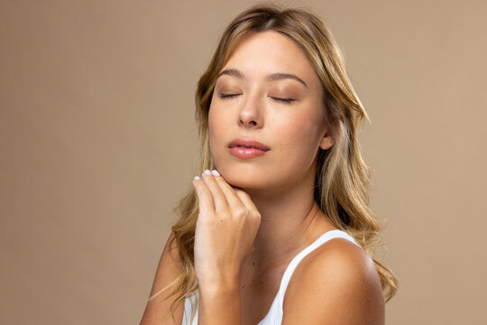 Caucasian woman wearing natural makeup and beige nail polish on beige background