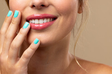 Fototapeta premium Caucasian woman wearing natural makeup and blue nail polish on beige background