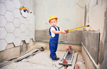 Child construction worker holding tape measure. Kid in safety helmet and work overalls standing by...