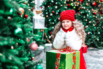 Gifts for Christmas and New Year, girl in a white fur coat and a red hat and skirt next to the Christmas Tree receives gifts outdoor, celebration and gifts