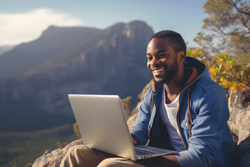 happy black man working remotely on laptop on mountain - obrazy, fototapety, plakaty