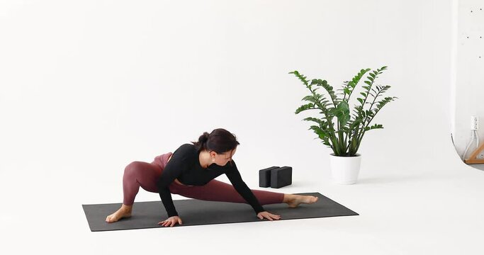 A woman practicing yoga performs rolls from one leg to another and does the Parivritta Janu Shirshasana exercise, tilting her head to her knee, training in sportswear while sitting on a mat
