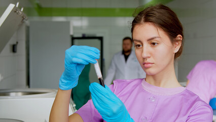 Young attractive female Caucasian doctor-cosmetologist demonstrates blood collection tube with centrifuged blood - separated platelet rich plasma - obrazy, fototapety, plakaty