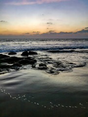 Obraz premium Sunset on Mandrem Beach in Goa, India. Bright and colorful sunset over the Indian Ocean, the Arabian Sea. A tropical beach with yellow sand and a bronze sunset.