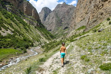 Naklejka premium A boy on the background of the picturesque gorge of the Jylgy-su river. The Caucasus Mountains near the ancient city of Eltuby. Next to the grotto with an ancient human parking lot.