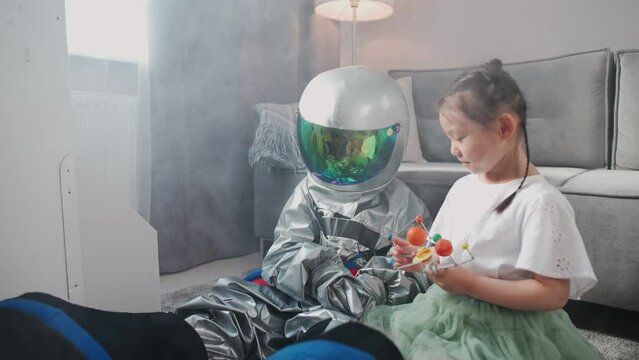 Asian kids play in the living room at home, a boy in an astronaut costume sitting on the floor with her sister, kids playing with a toy model of the solar system, slow motion.