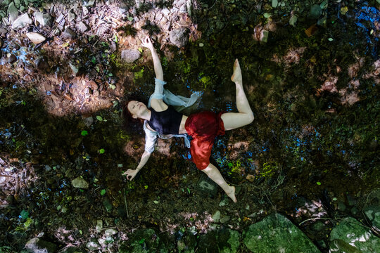 happy sexy sensual woman lies happily extatic while forest bathing in the shallow water of a forest mountain stream