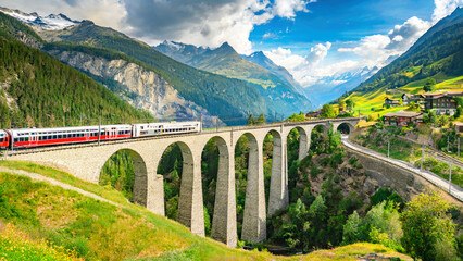 Train moves on railroad bridge in mountain, spring landscape. Switzerland. Red train of Bernina Express on railroad bridge in mountains. - obrazy, fototapety, plakaty