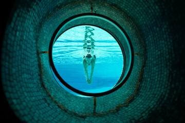 Woman Swimming in the Ship Porthole in Underwater in Swimming Pool in a Sunny Day in Switzerland.